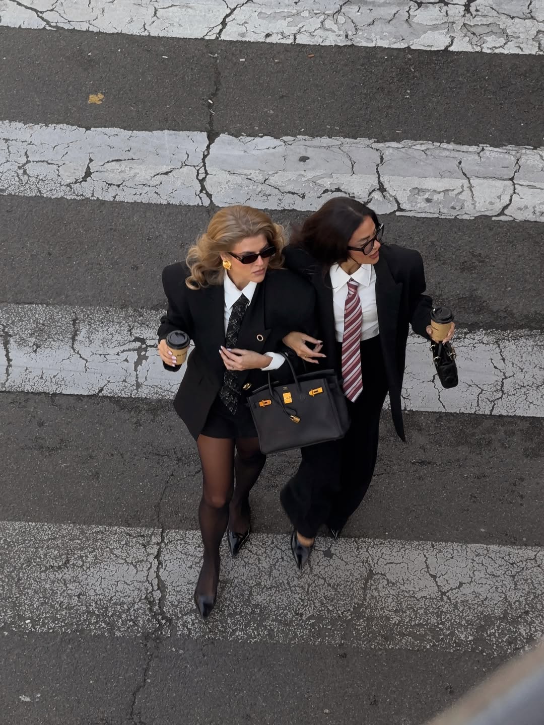 Two women in black blazers and sunglasses crossing the street with a black handbag